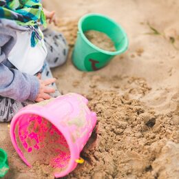 Kleines Kind spielt mit Sand und Eimern im Sandkasten